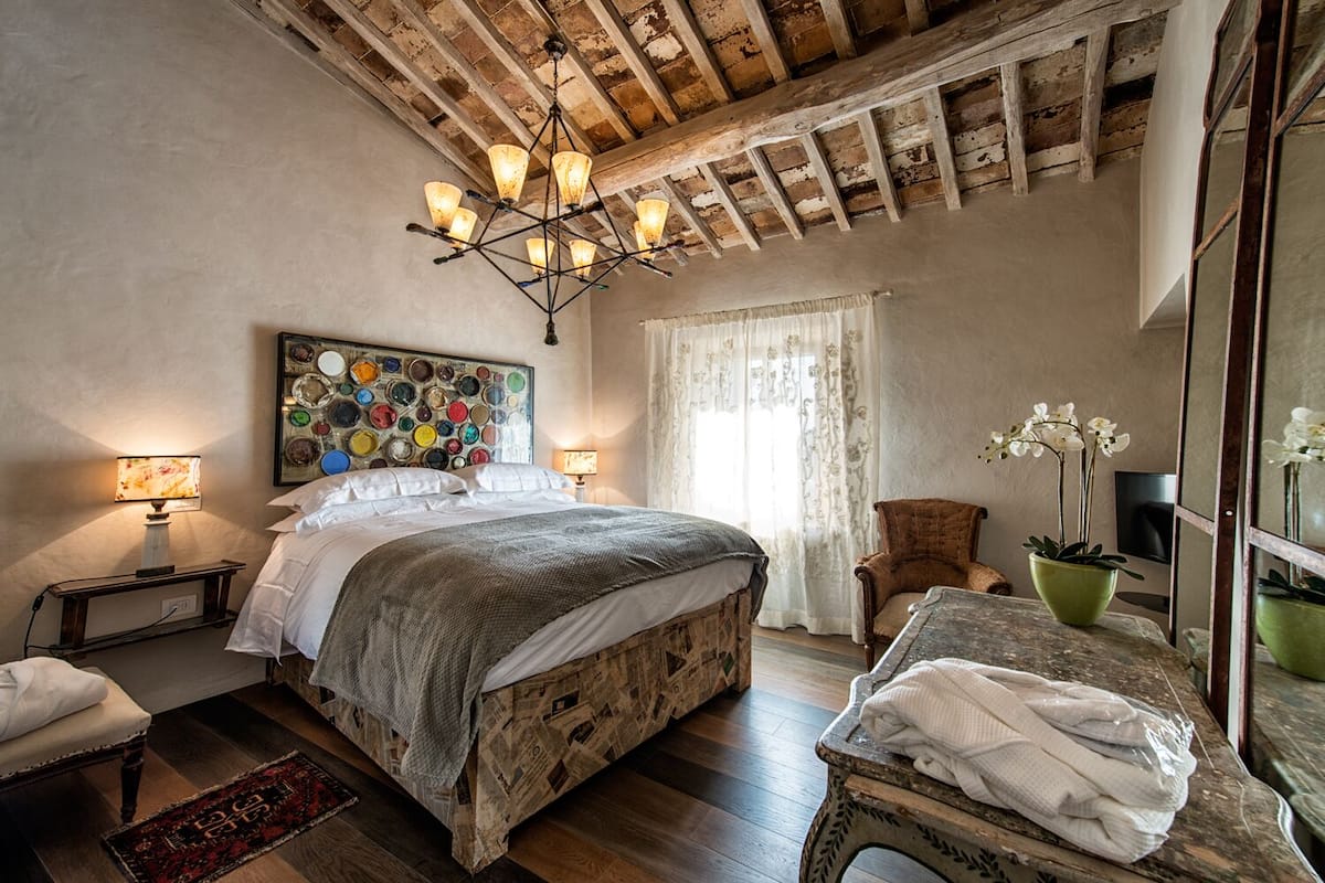 Un dormitorio con una cama de madera, una araña, un cuadro en la pared y una ventana con cortinas.