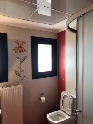 A bathroom with a toilet, a radiator, a window, and a wall-mounted toilet paper holder. - Charming 2-bed House in Kallithea (Zakynthos)