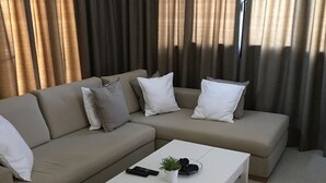 A modern living room with a beige sectional sofa, white cushions, a white coffee table, and a small potted plant. - Charming 2-bed House in Kallithea (Zakynthos)
