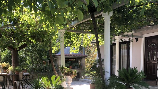 A well-maintained outdoor patio area with a stone table and chairs, surrounded by lush greenery and potted plants. - Charming 2-bed House in Kallithea (Zakynthos)