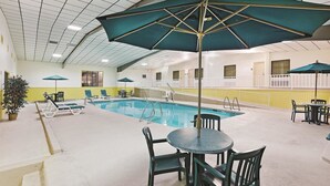 An indoor swimming pool with lounge chairs and umbrellas, surrounded by yellow walls and a tiled ceiling. - Motel6 Bartlesville OK (Bartlesville)