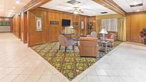 A spacious lobby with wooden paneling, a patterned carpet, and a seating area with chairs and a sofa. - Motel6 Bartlesville OK (Bartlesville)