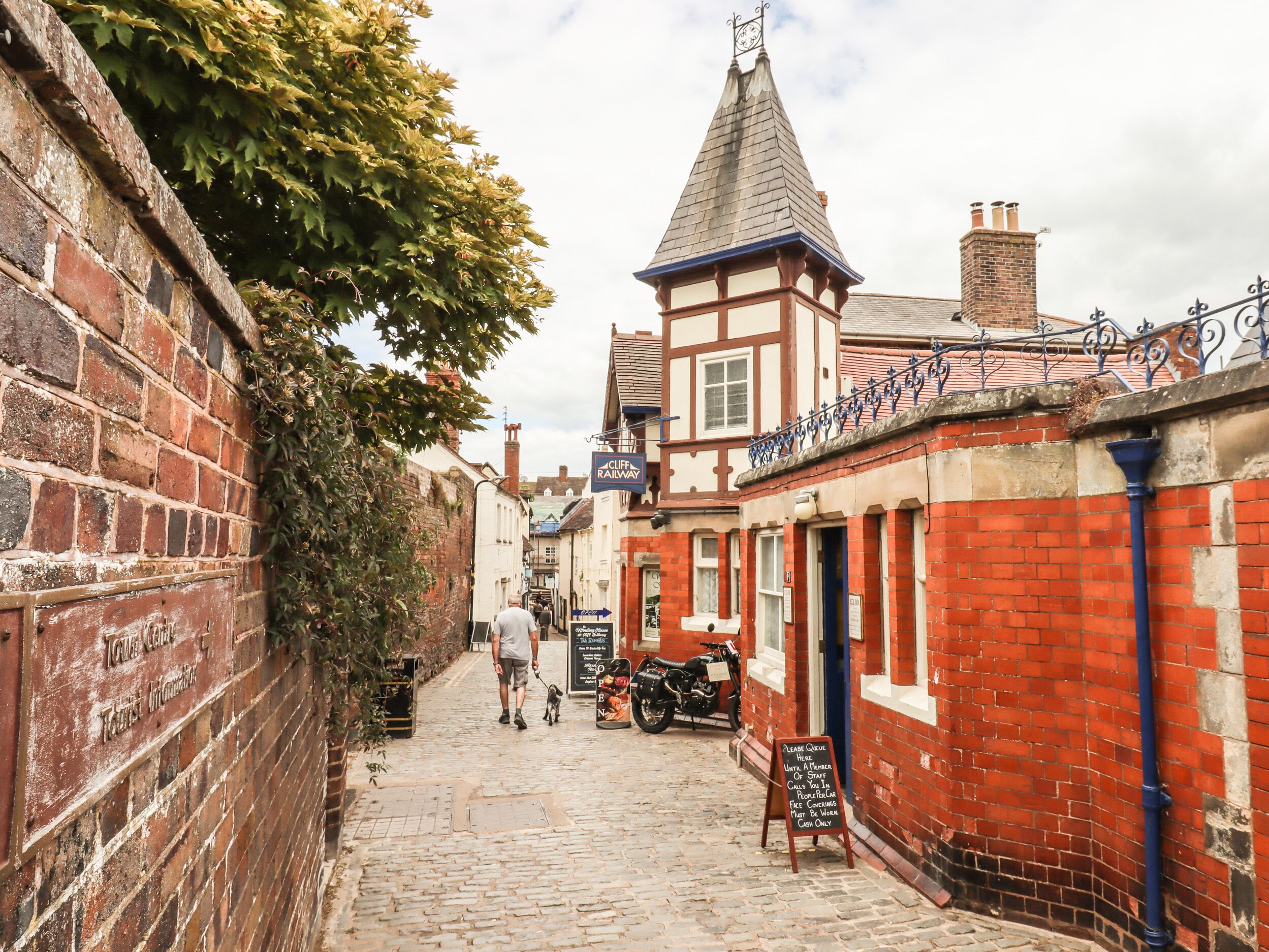 Une ruelle étroite pavée, bordée de bâtiments historiques, dont une gare et un pub.