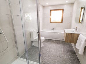 A modern bathroom with a glass shower enclosure, a bathtub, a toilet, and a sink with a wooden vanity. - Traeannagh Bay House (Lettermacaward)