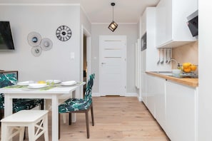 Et moderne køkken med hvide skabe, en træbordplade og et spiseområde med et hvidt bord og stole.