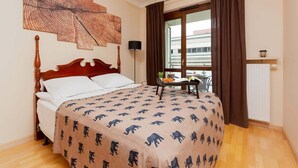 Une chambre à coucher avec un lit, une œuvre d’art murale, une table avec une plante et une fenêtre avec des rideaux.