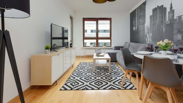 Un salon moderne comprenant un canapé, une table à manger et des chaises, un téléviseur et un tapis à motifs.