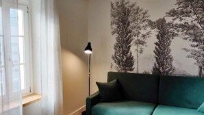 Una habitación con un sofá verde azulado, una lámpara de pie y una ventana con cortinas de gasa.