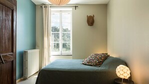 Une chambre à coucher avec un lit, une table de chevet avec une lampe, une fenêtre avec des rideaux et un radiateur.