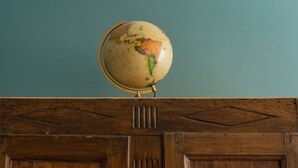 Un globe terrestre posé sur un meuble en bois, devant un mur de couleur turquoise.