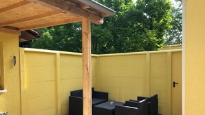 A covered patio area with yellow walls, a wooden pergola, and outdoor seating.