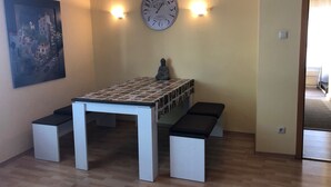 A room with a white table and benches, a clock on the wall, and a Buddha statue.