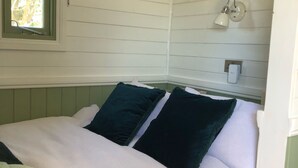 A bedroom with a bed, pillows, a window, and a wall-mounted lamp. - A beautiful Railway Carriage, with stunning views & use of the Ndoro Pool. (Chippenham)
