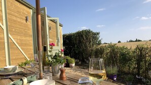 A wooden table set for dining with a wine glass and a bowl, surrounded by potted plants and a wooden building in the background. - A beautiful Railway Carriage, with stunning views & use of the Ndoro Pool. (Chippenham)