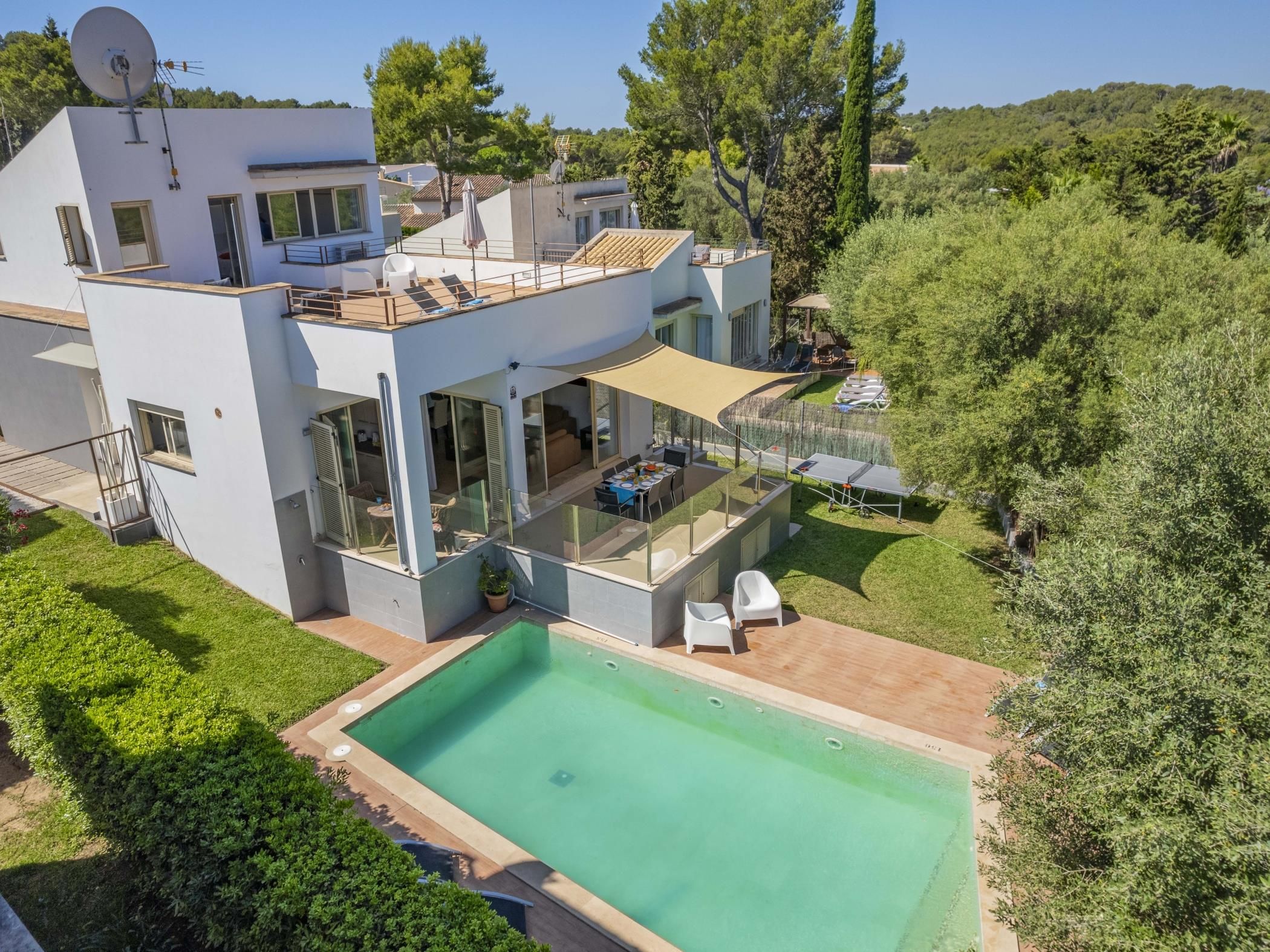 A modern two-story house with a swimming pool, outdoor seating, and a large glass window.
