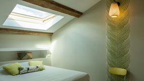 Ein Schlafzimmer mit Oberlichter, einem Bett mit Kissen, einem Nachttisch und einer Wandlampe.
