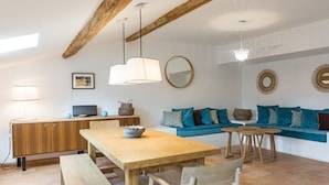 Ein gemütlicher Wohnbereich mit einem Holztisch, Bänken, einer blauen Couch und einem Fernseher auf einer Holzkommode.