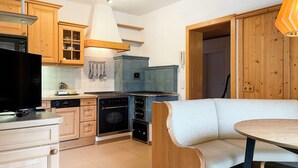 A kitchen with wooden cabinets, a built-in oven, a dining area with a bench, and a hanging light fixture. - Dormio Gasthof Höllwirt (Obertraun)