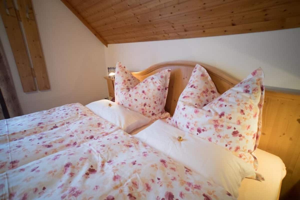 A bedroom with a wooden ceiling, a bed with floral bedding, and a nightstand with a lamp.