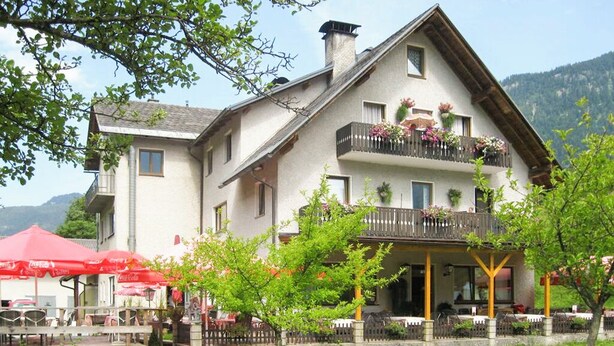 A two-story building with balconies, a covered outdoor seating area, and a garden. - Dormio Gasthof Höllwirt (Obertraun)