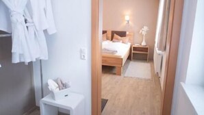 A hotel room with a wooden floor, a bed with a headboard, a bedside table, a nightstand, and a wall-mounted robe rack. - Dormio Gasthof Höllwirt (Obertraun)