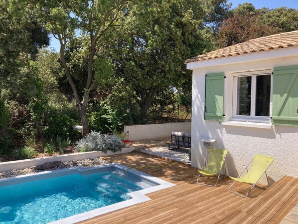 Una piscina con una terraza de madera, una pequeña mesa y una silla.