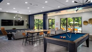 A pool table in a room with a dining area, large windows, and a view of outdoor furniture.