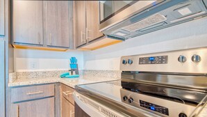 A kitchen with stainless steel appliances, wooden cabinets, and a granite countertop. - Walk to UF | Stylish 2BR | Ideal for Hospital & Gator Visitors (Gainesville)