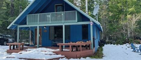 A cabin with a balcony, a covered porch, and a snow-covered ground.