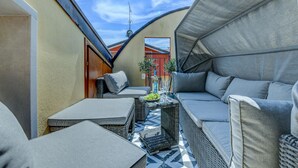 Un espace extérieur aménagé avec des meubles en osier, un tapis à motifs et une petite table sur laquelle sont disposés un saladier de fruits et des boissons.