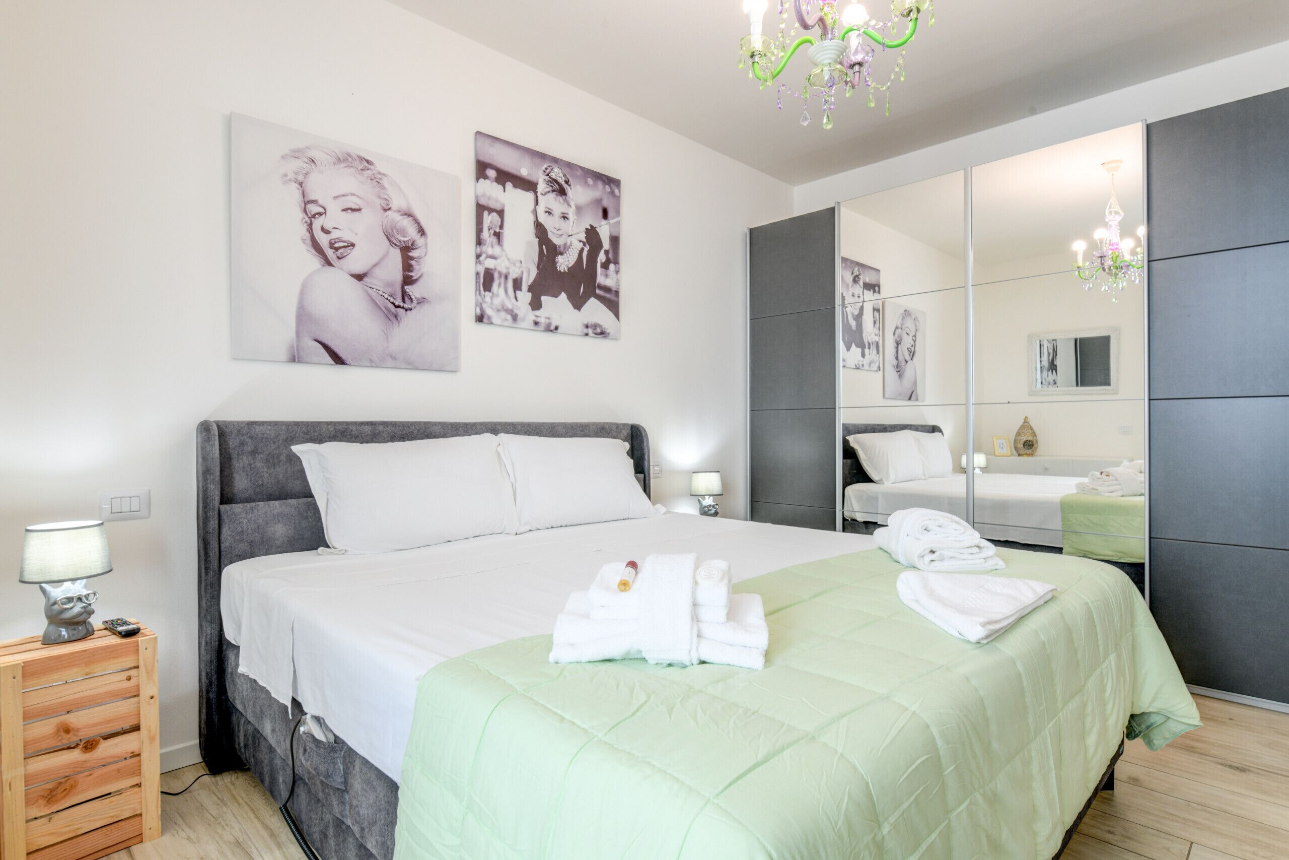 A modern bedroom with a large bed, a nightstand, a mirror, and artwork on the wall.