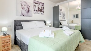 Une chambre à coucher moderne avec un grand lit, une table de chevet, un miroir et des œuvres d’art accrochées au mur.