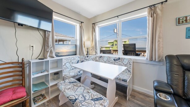Een gezellige kamer met een witte tafel en bankje, een houten stoel, een zwarte lederen fauteuil en een boekenplank.