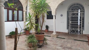 A courtyard with potted plants, a tiled floor, and a decorative gate.