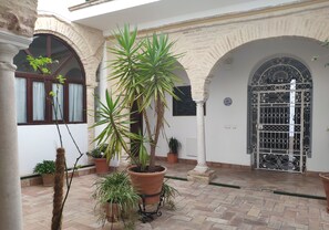 A courtyard with potted plants, a tiled floor, and a decorative gate.