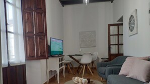 Ein Wohnzimmer mit einer Couch, einem Glastisch, einem Fernseher und einem Essbereich mit Stühlen und Tisch.