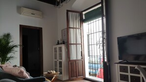 Ein Wohnzimmer mit einer Couch, einem Fernseher, einer Kommode und einem Fenster mit Blick auf ein Auto draußen.