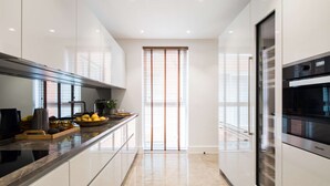 A modern kitchen with a sleek design, featuring a long countertop, built-in appliances, and a large window with blinds.