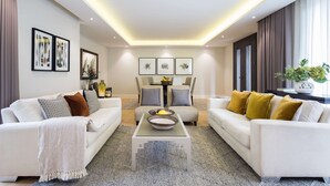 A modern living room with two white sofas, a glass coffee table, and a dining table with chairs.