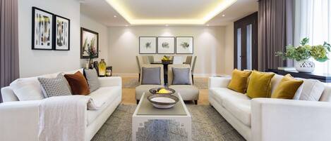 A modern living room with two white sofas, a glass coffee table, and a dining table with chairs.