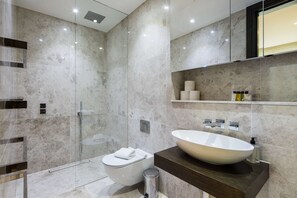 Ein modernes Badezimmer mit einer gläsernen Dusche, einer weißen Toilette und einem großzügigen Waschtisch auf einer dunklen Ablagefläche.