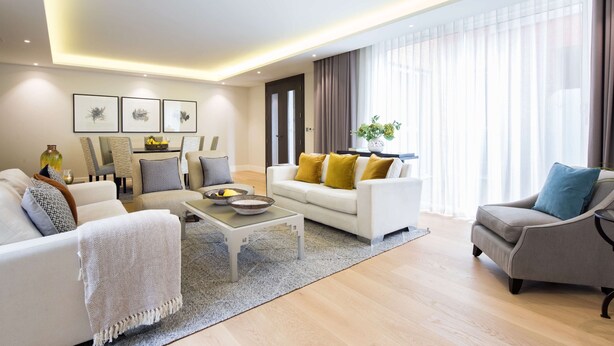 A modern living room with a white sofa, grey armchair, and a coffee table. There are framed pictures on the wall and a plant on a side table.