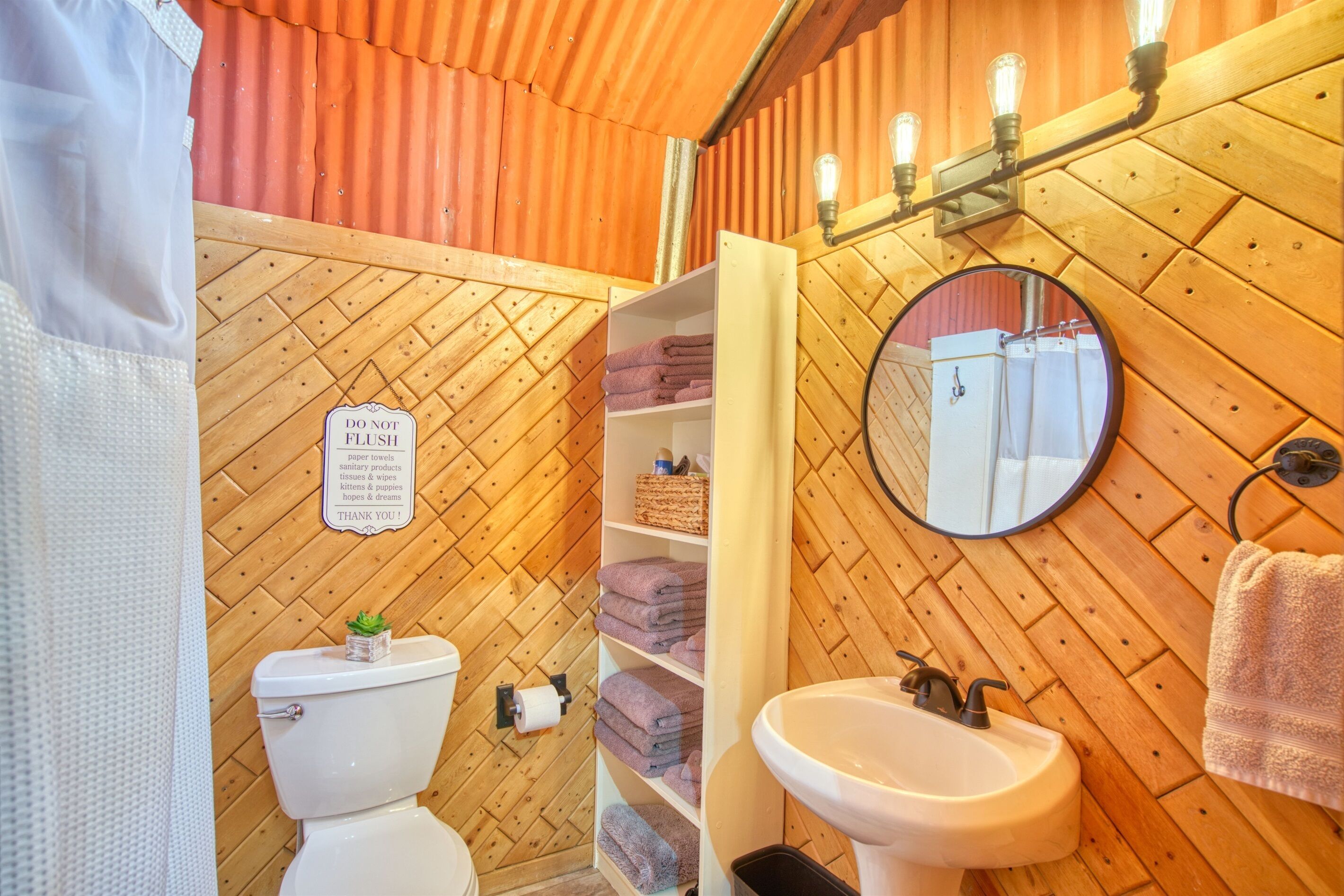 A bathroom with a wooden wall, a toilet, a sink, and shelves with towels.