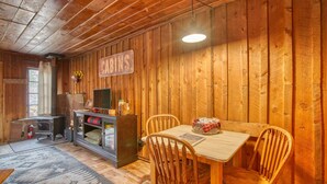 A cozy cabin interior with a wooden dining table, chairs, a small kitchen area, and a sign that reads "CABINS". - Rustic Riverside Cabin with Patio — Family Escape (Lyons)