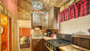 A compact kitchen with wooden cabinetry, a gas stove, a microwave, and a small sink. - Rustic Riverside Cabin with Patio — Family Escape (Lyons)