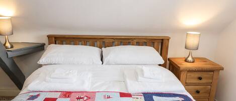 A neatly made bed with white linens and a red, white, and blue quilt. There are two wooden nightstands with lamps on either side of the bed.