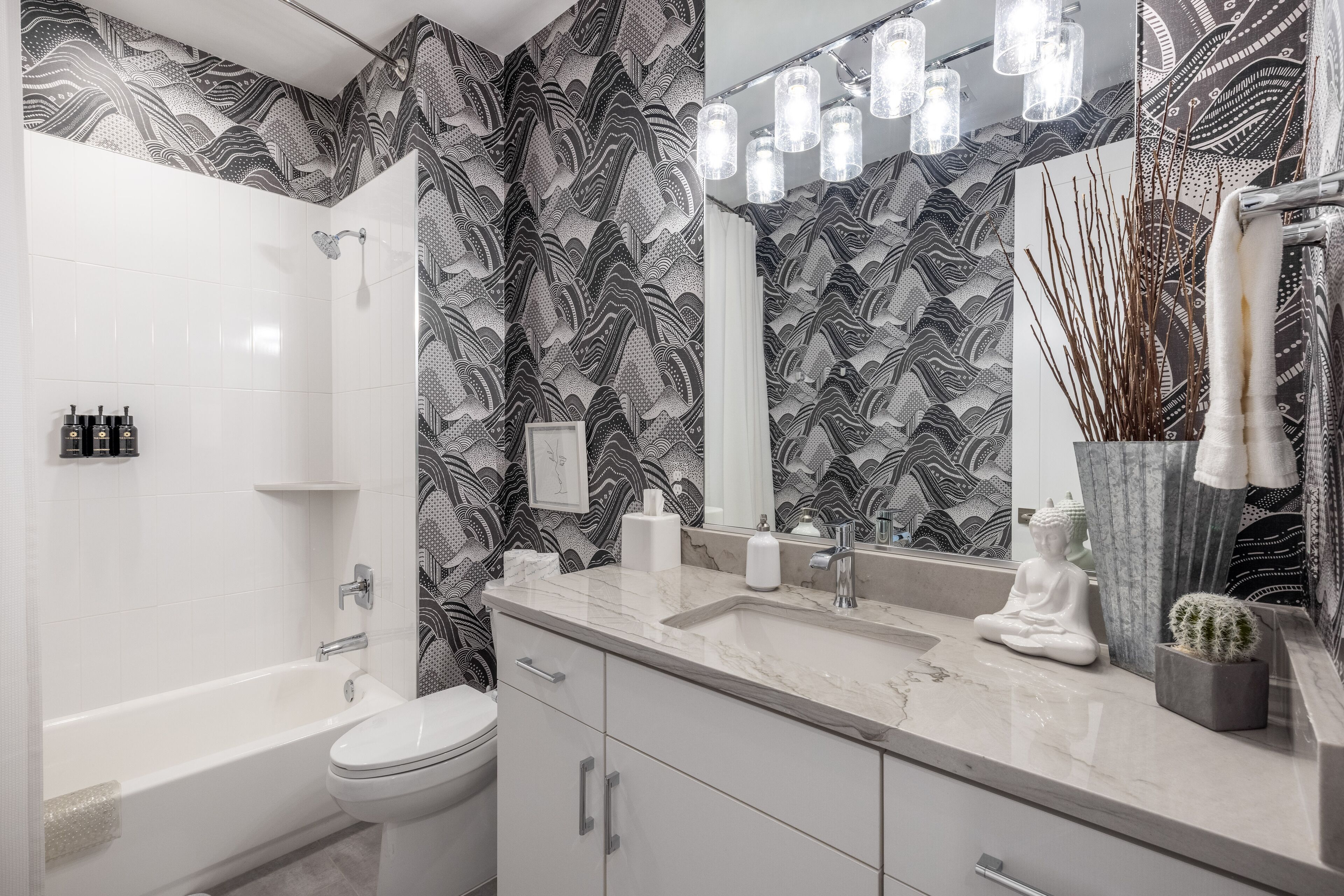 A modern bathroom with a large mirror, a bathtub, a toilet, and a sink.