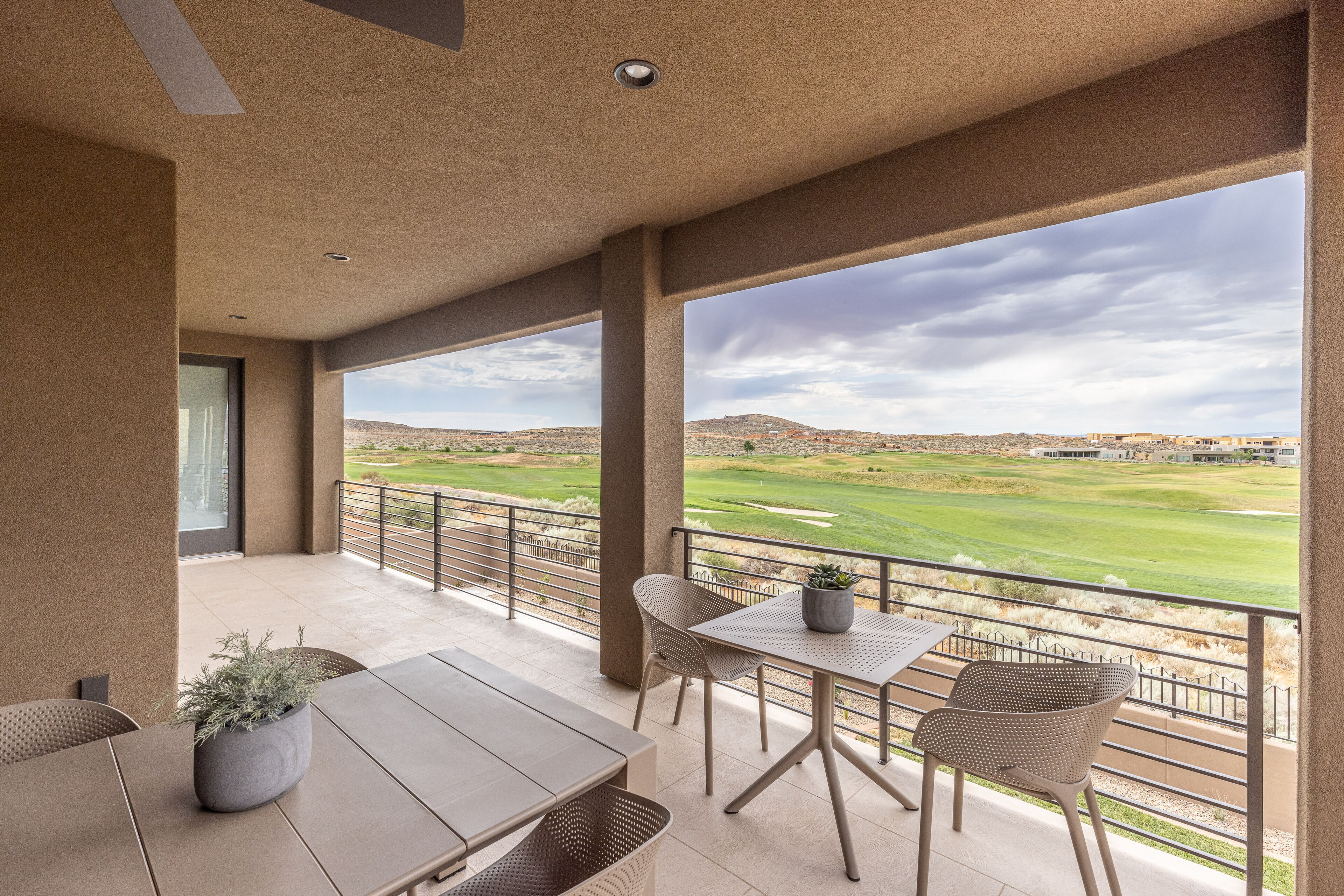 A balcony with a view of a golf course, a table, chairs, and a potted plant.