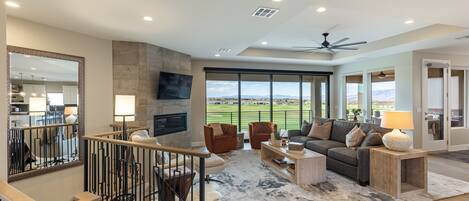 A spacious living room with a large window, a fireplace, and a modern ceiling fan.