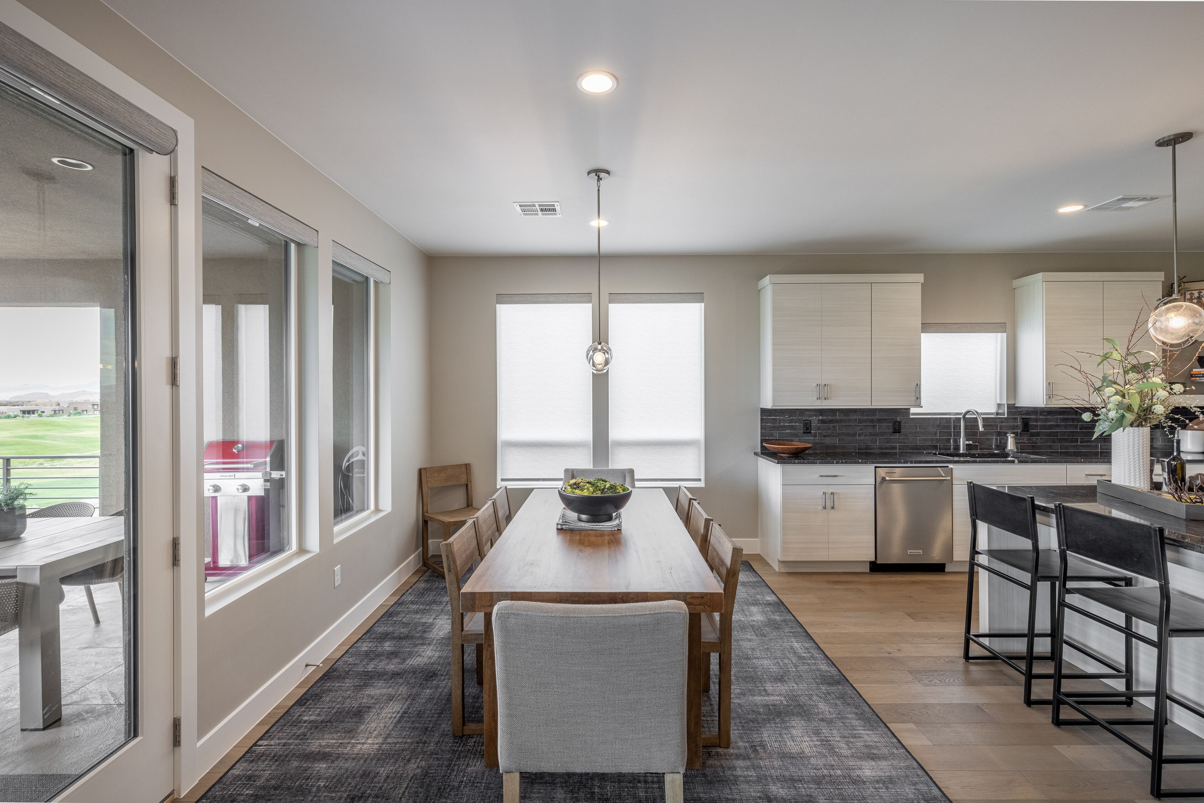 A modern kitchen with a dining area, large windows, and a view of the outdoors.